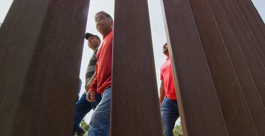 A view of three men walking near the border fence.