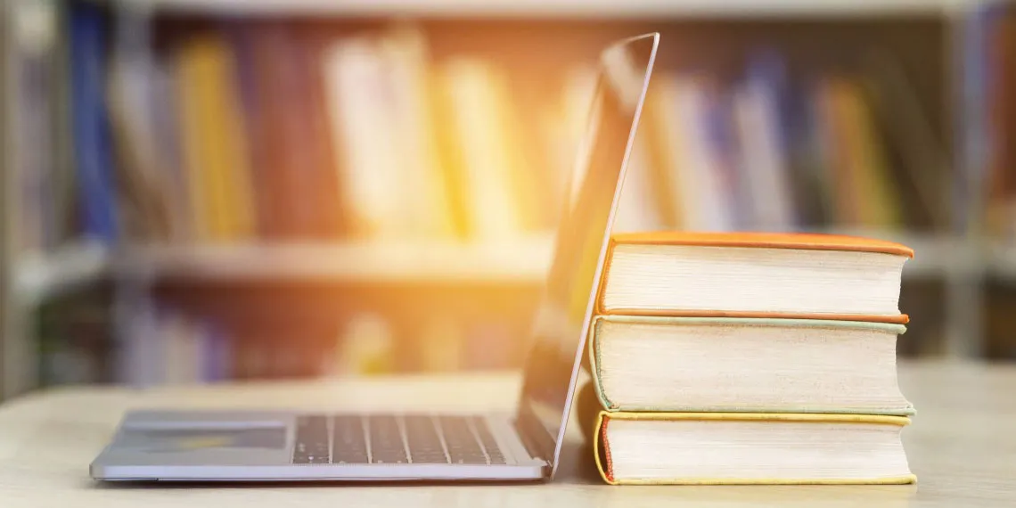 An open laptop next to a stack of books.