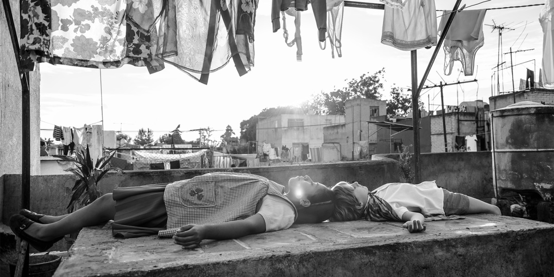 A still from Alfonso Cuarón's film, Roma, featuring two of the characters laying on a slab of concrete. 