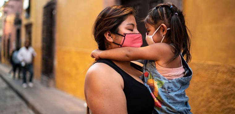 A woman and child wearing masks hug each other.