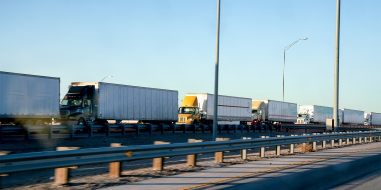 A line of semi-trucks on the highway driving towards the border from the U.S. to Mexico.